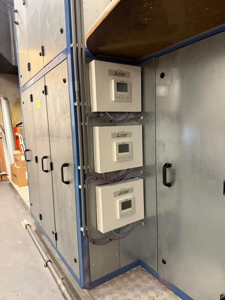 Drie regelunits met display onder elkaar op de zijkant van een luchtbehandelingskast, netjes bekabeld