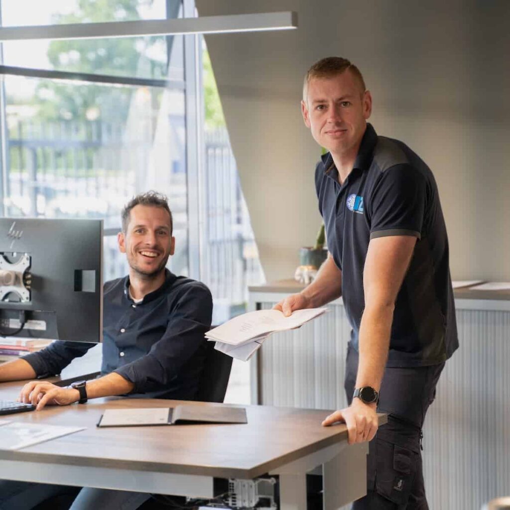 Monteur van TIZ overhandigt werkbonnen aan een collega achter het bureau op kantoor